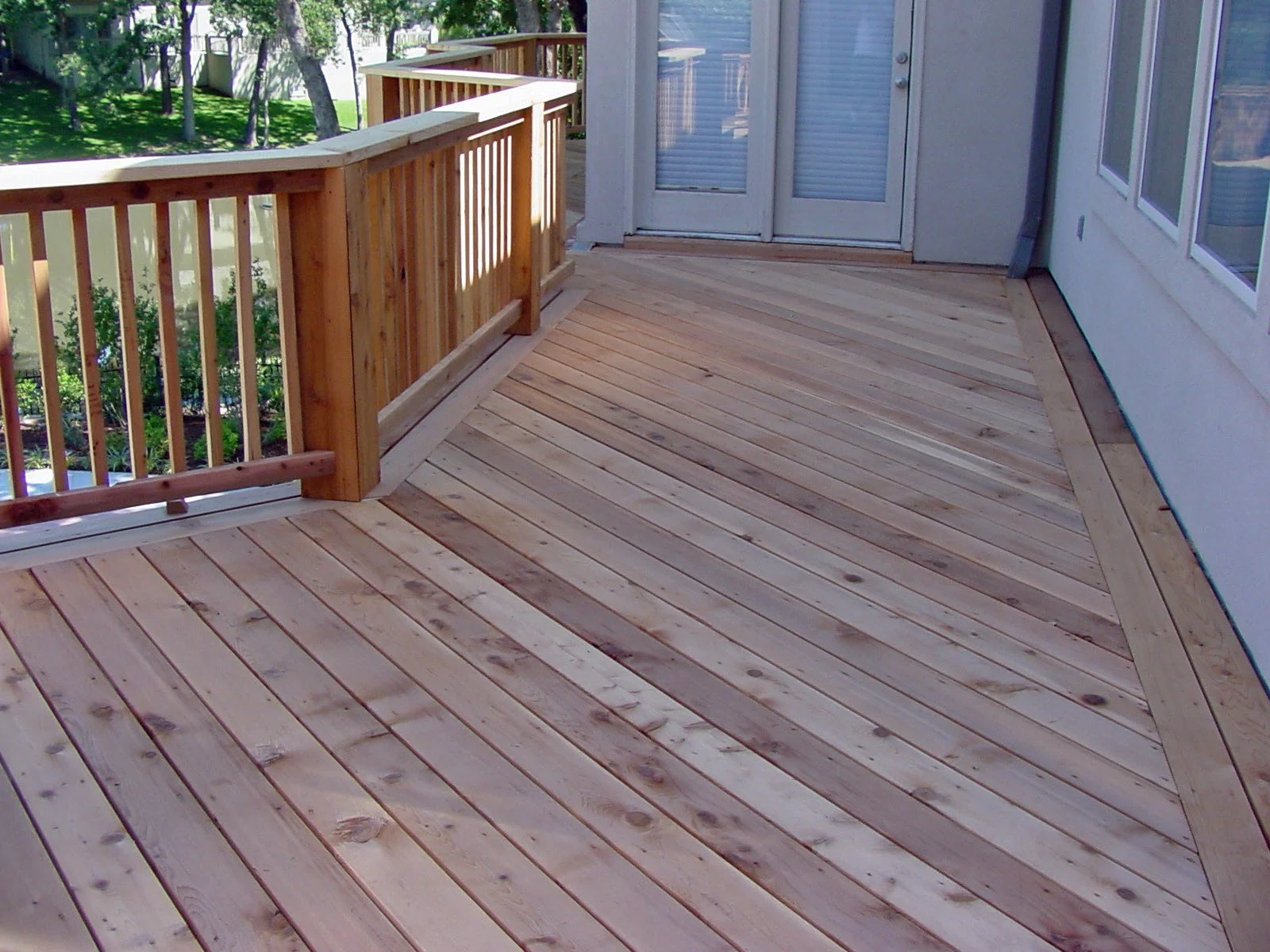 A new wooden deck with a railing attached to a house, featuring multiple wood planks and a sliding glass door leading inside.