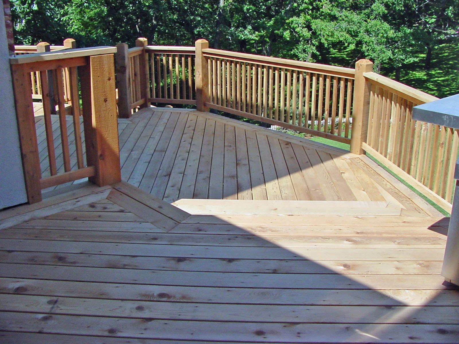 A wooden deck with a railing overlooks a wooded backyard with lush green trees.