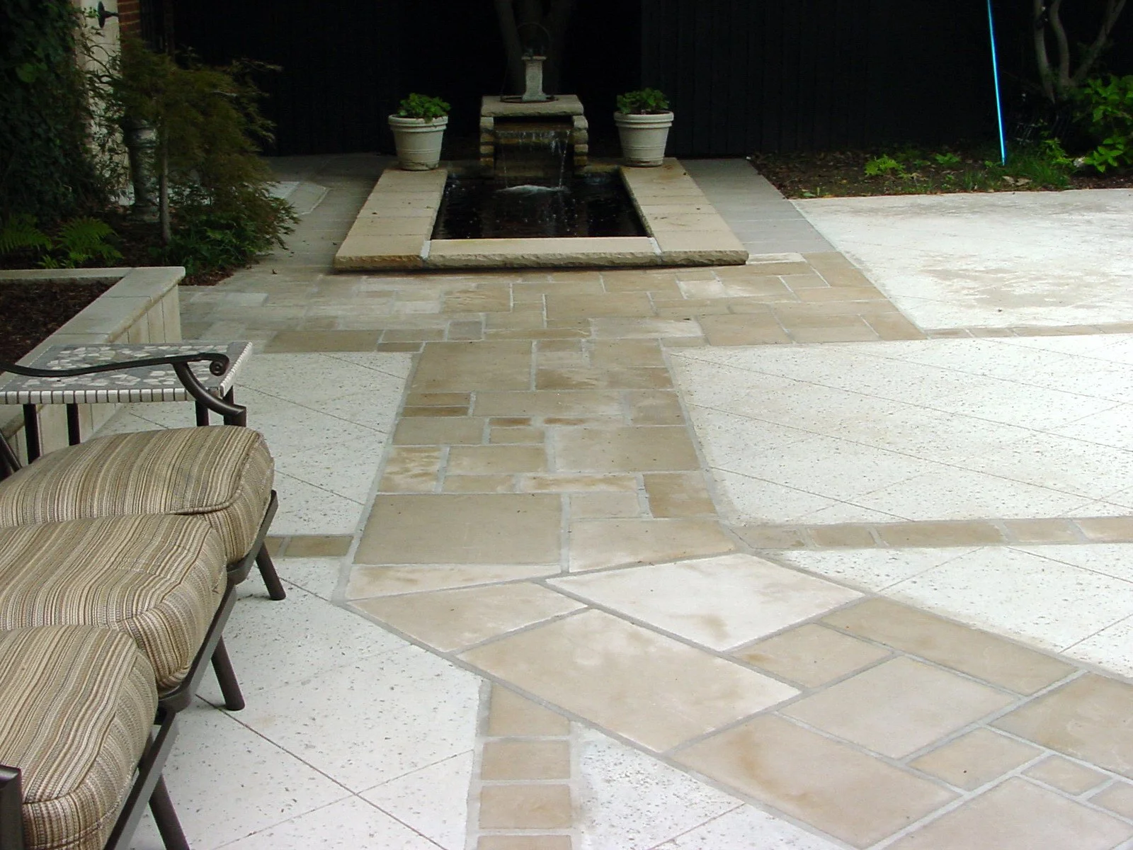 Outdoor patio area with a decorative water fountain, potted plants, and a bench with cushions.