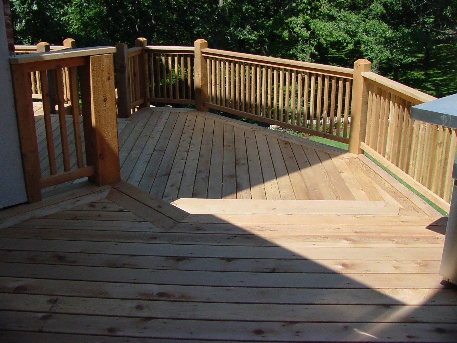 Wooden deck with a railing overlooking a lush green forest.