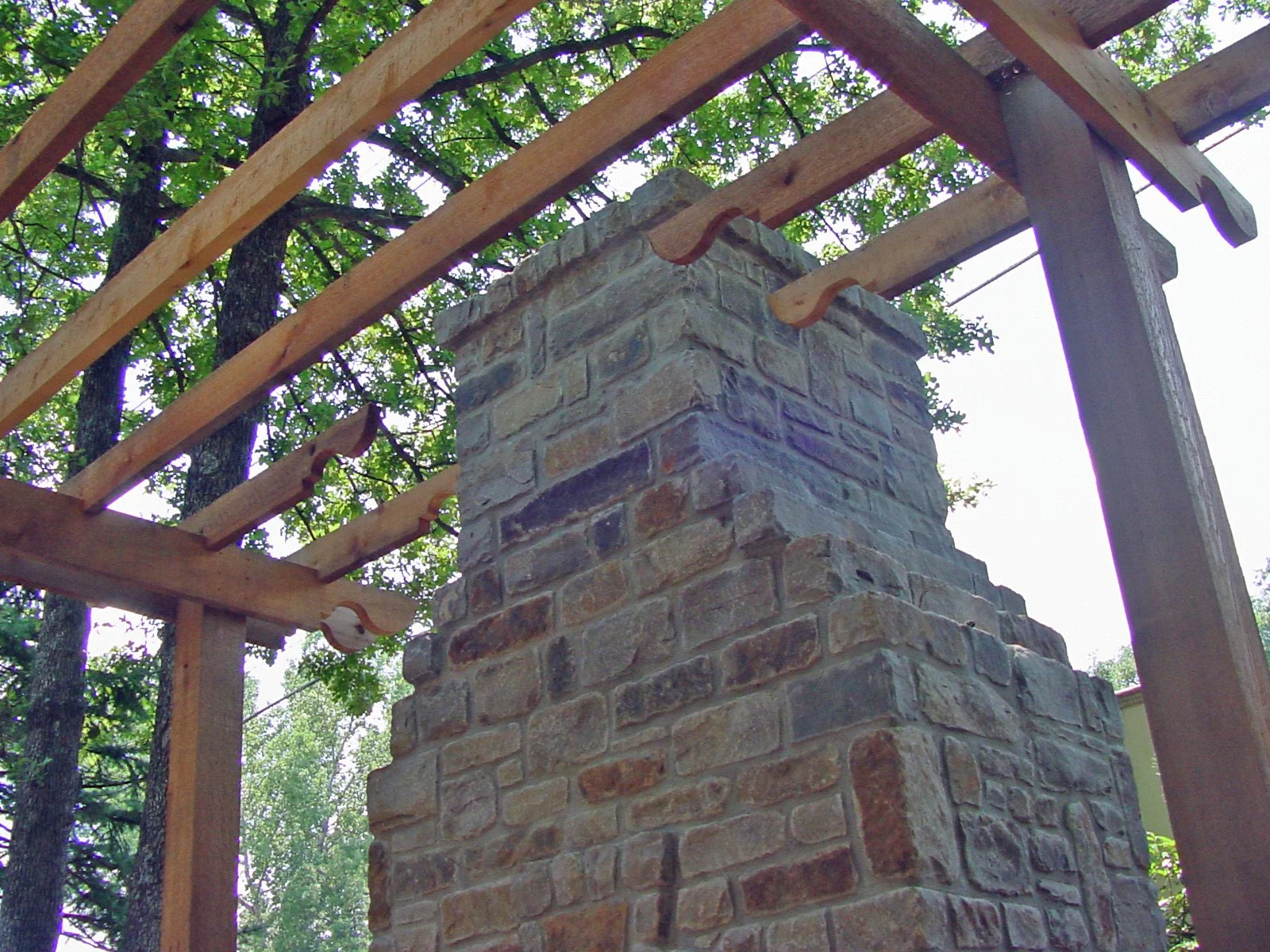 A brick chimney under construction with wooden framing around it, and trees in the background.