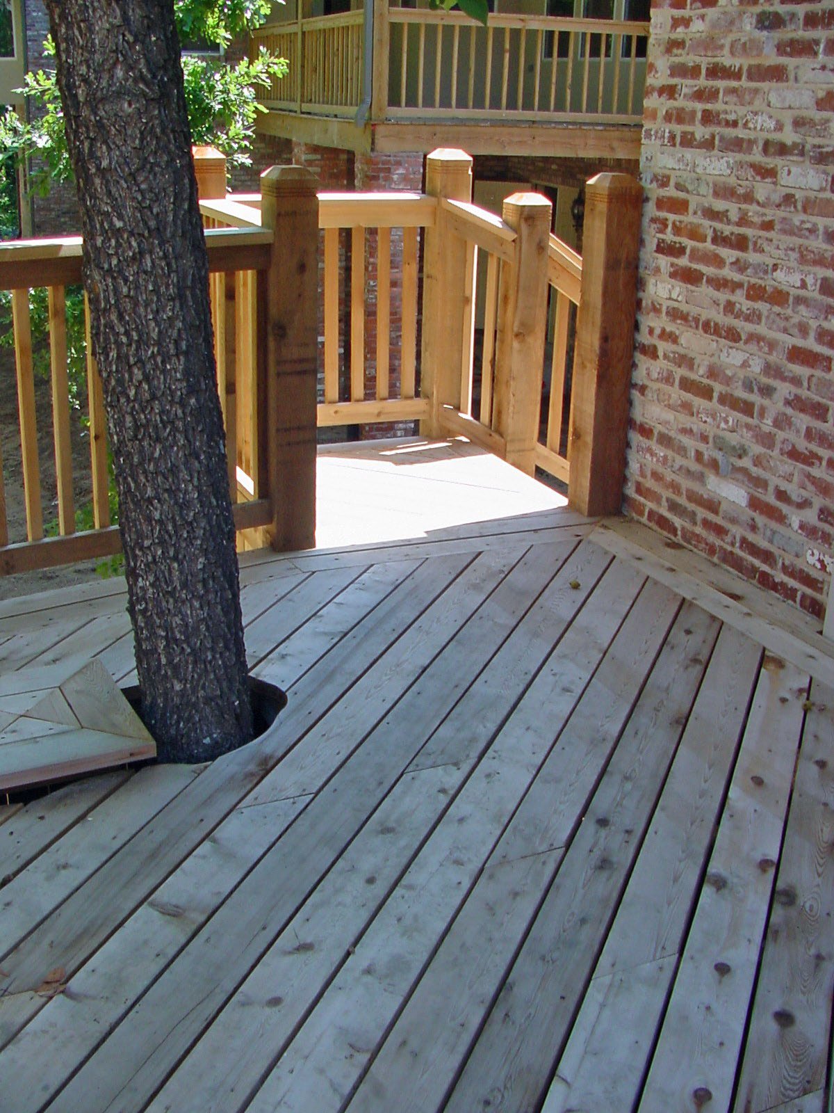A wooden deck with a tree growing through it, surrounded by new wood railing, and adjacent to a brick wall.