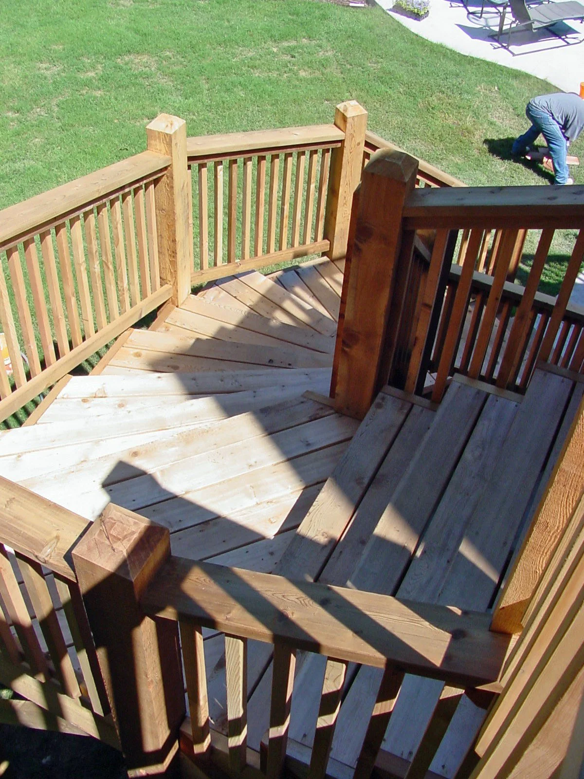 Wooden stairs leading down to a grassy backyard, with a person working in the distance.