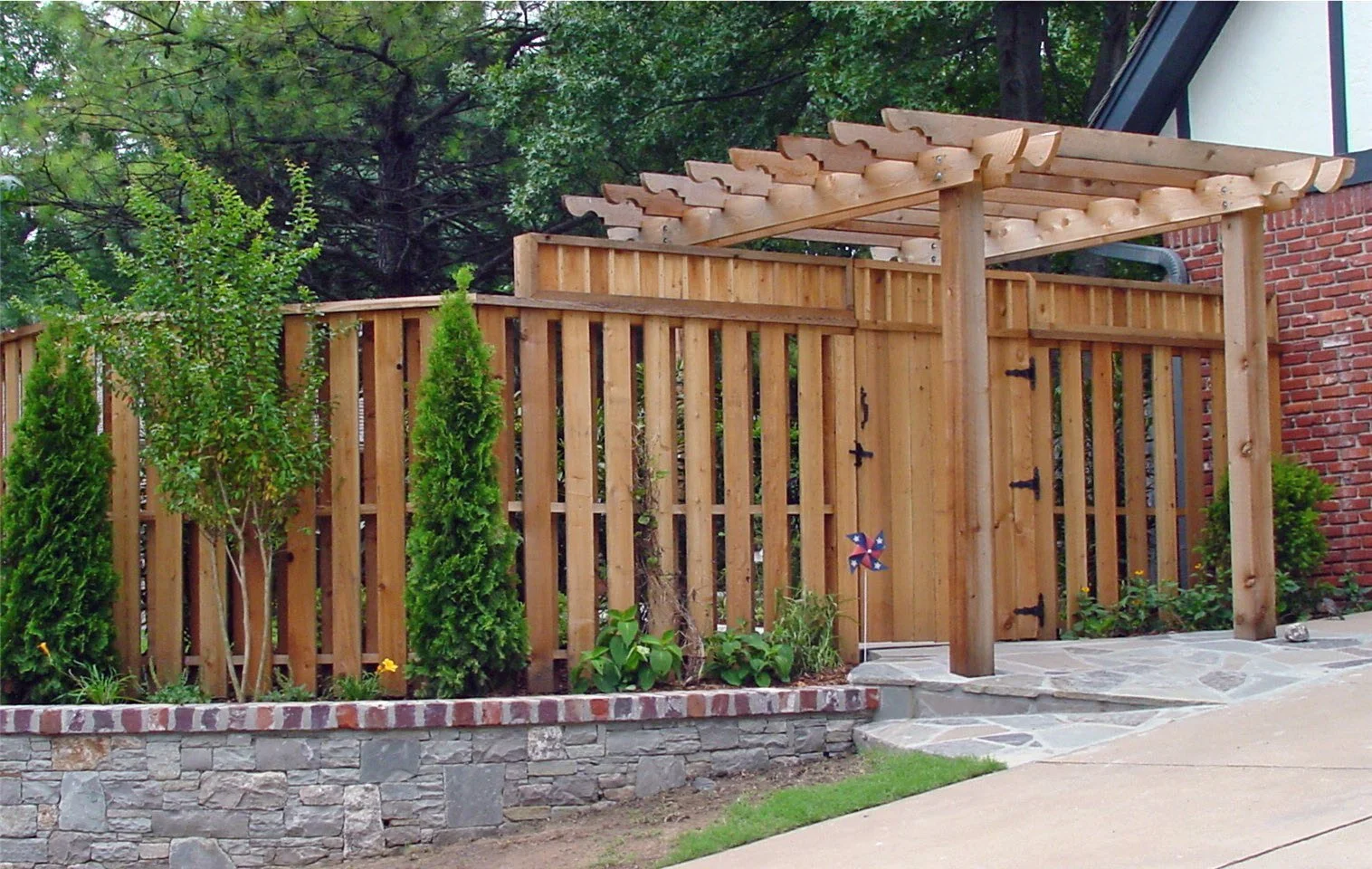 Wooden backyard fence with gate, stone pathway, small shrubs, and trees in the background.