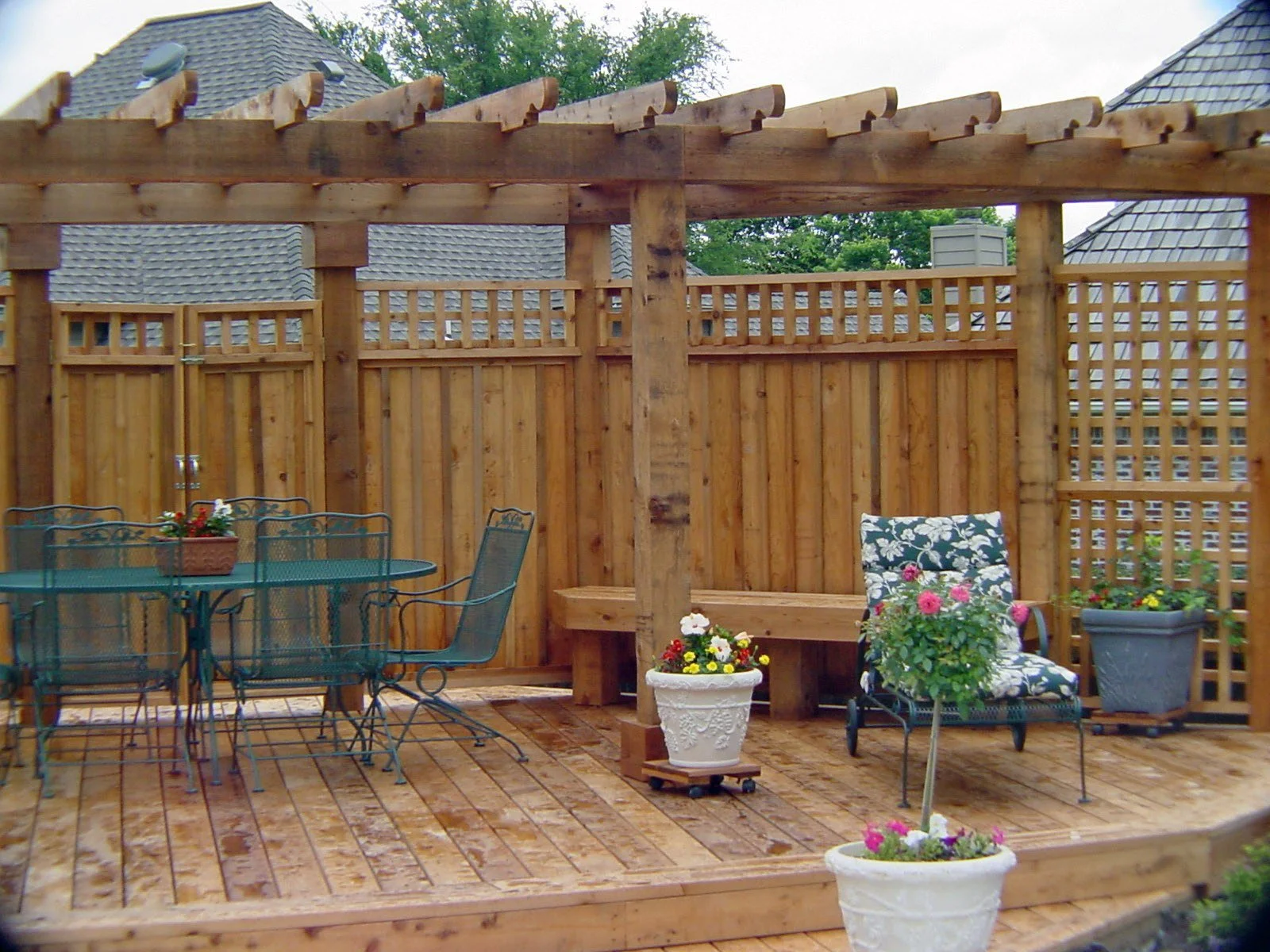 A wooden outdoor patio with a table and chairs, flower pots, and a lattice fence.