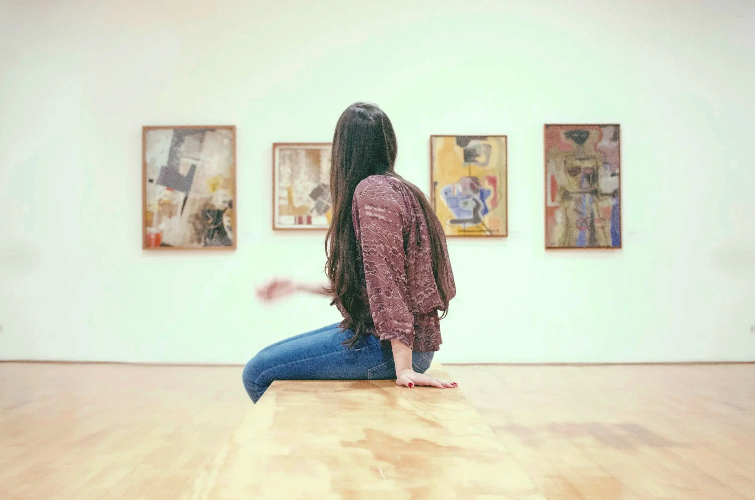 Nainen esittelee taideteoksia museossa, kääntyy sivulle ja istuu pöydän päällä.