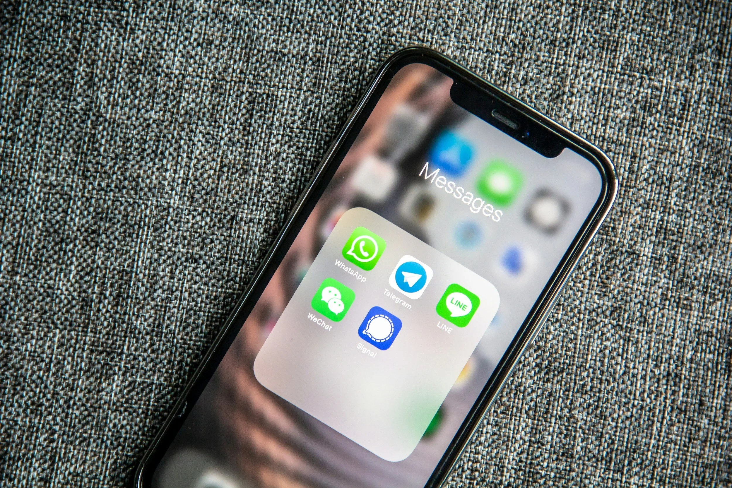 Close-up of a smartphone screen displaying messaging app icons, resting on a textured gray fabric surface.