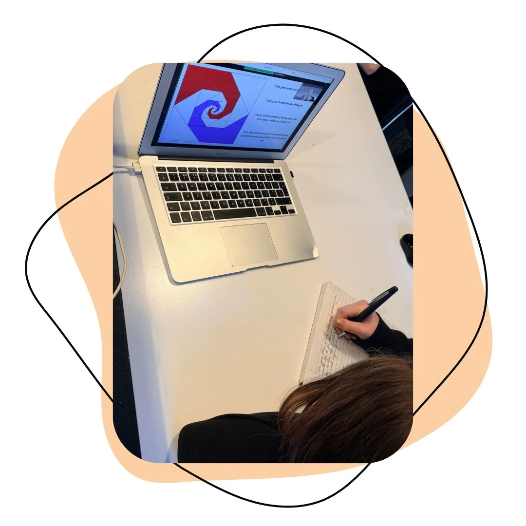 Open laptop displaying a spiral geometric logo and a presentation slide, with a person writing notes on a notepad next to it on a white table.