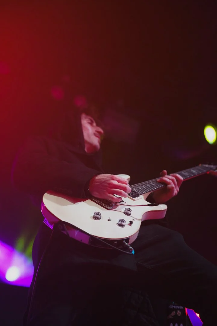 A person playing an electric guitar on stage, with colorful stage lights in the background.