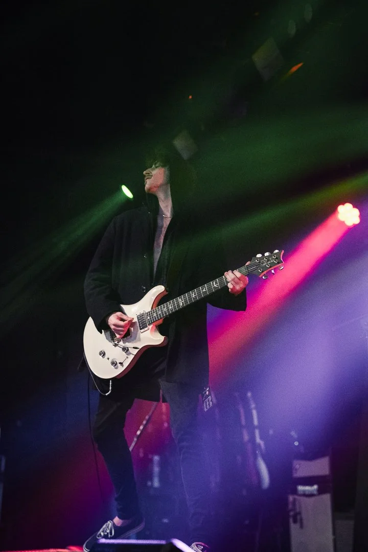 Musician playing an electric guitar on stage under colorful lights.