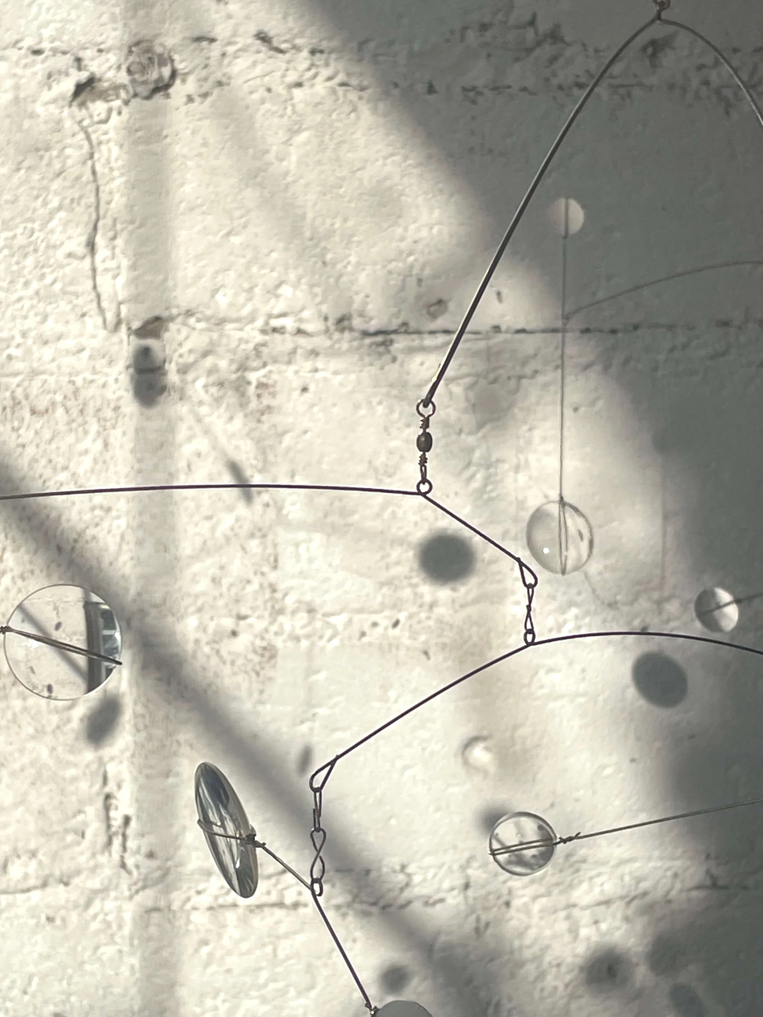 Une sculpture murale moderne composée de cercles métalliques suspendus par des fils, projetant des ombres sur un mur blanc avec des marques ou des peintures.