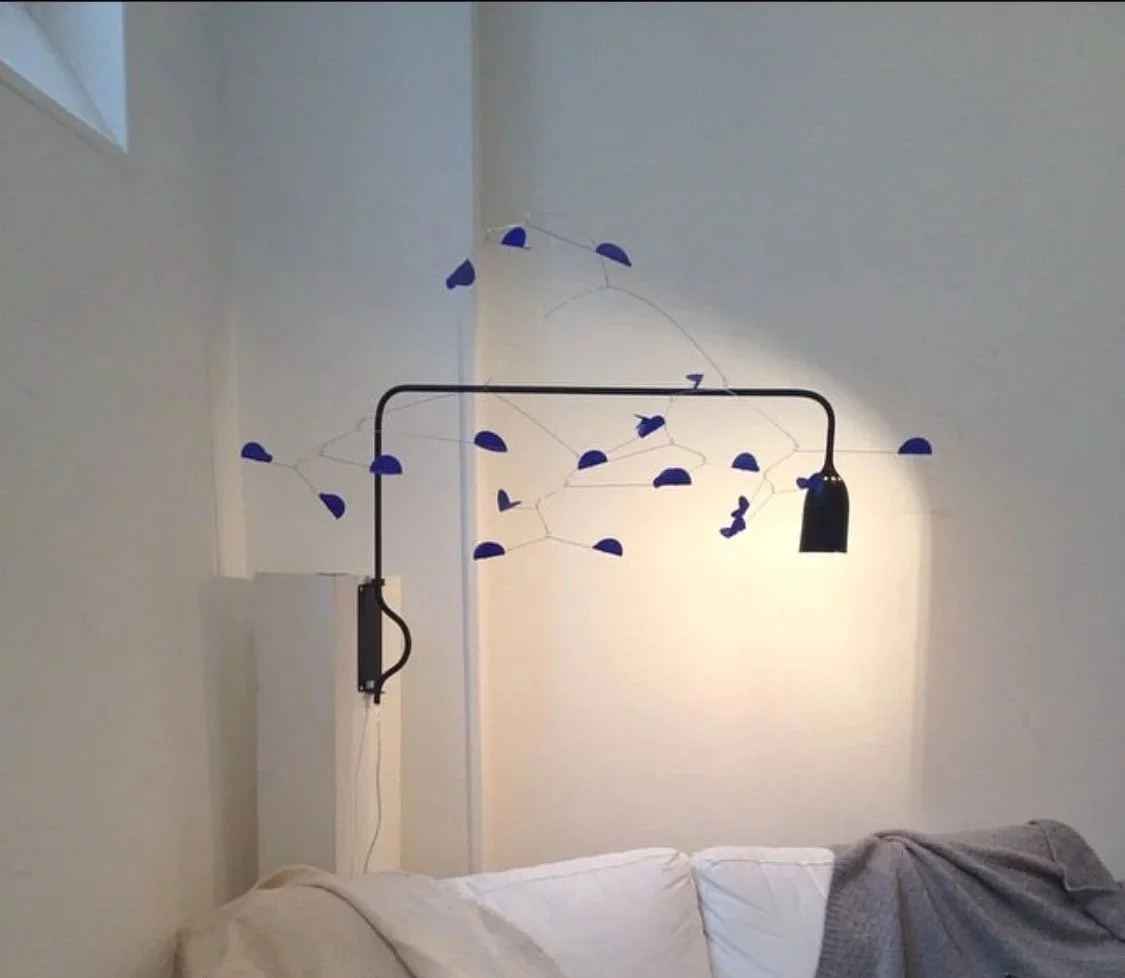 Une lampe suspendue originale avec un bras noir et des éléments en forme de demi-lune bleue suspendus autour, créant un design artistique dans une chambre.