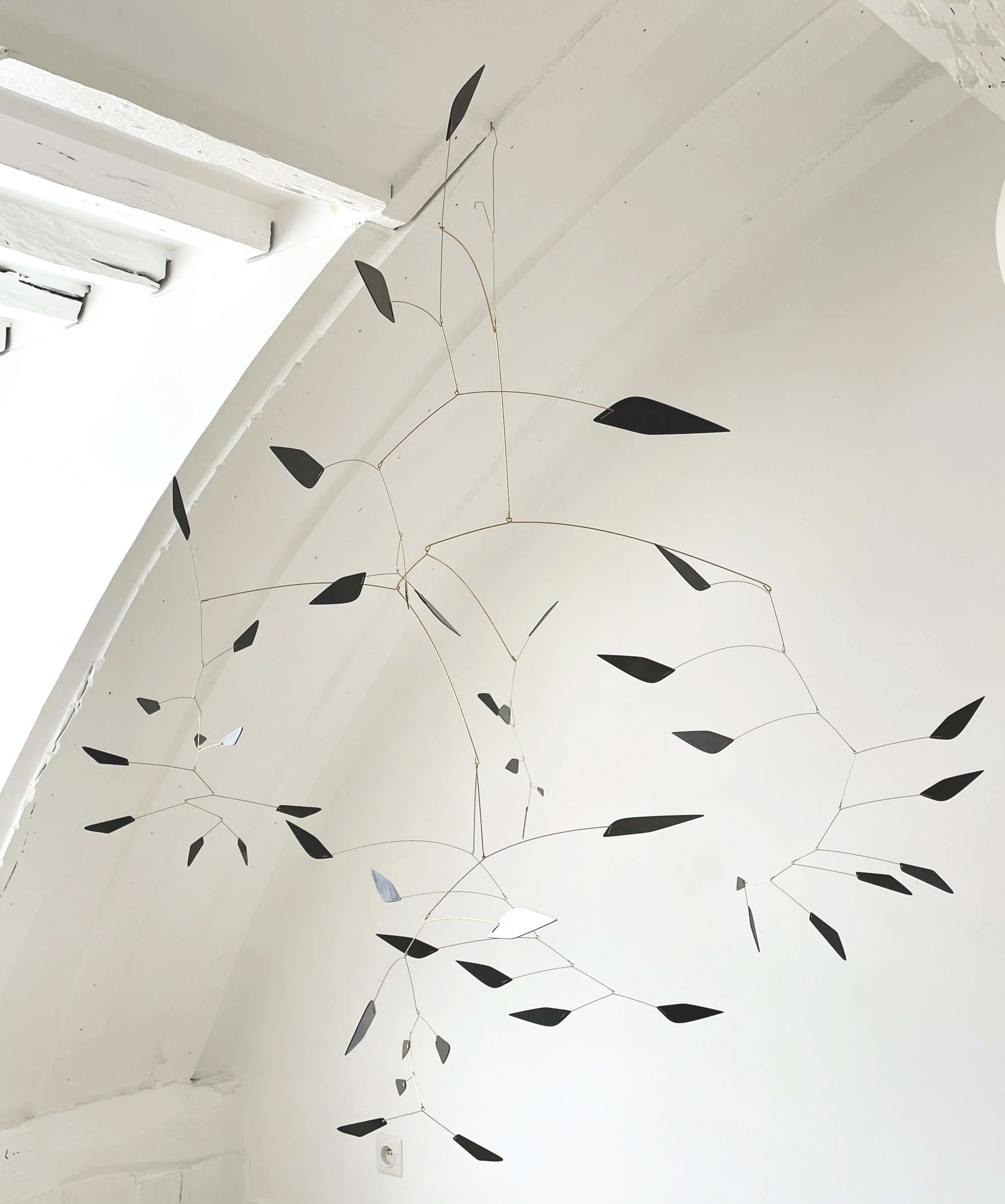 Lampe suspendue moderne avec des éléments en forme de feuilles noires suspendus au plafond blanc.