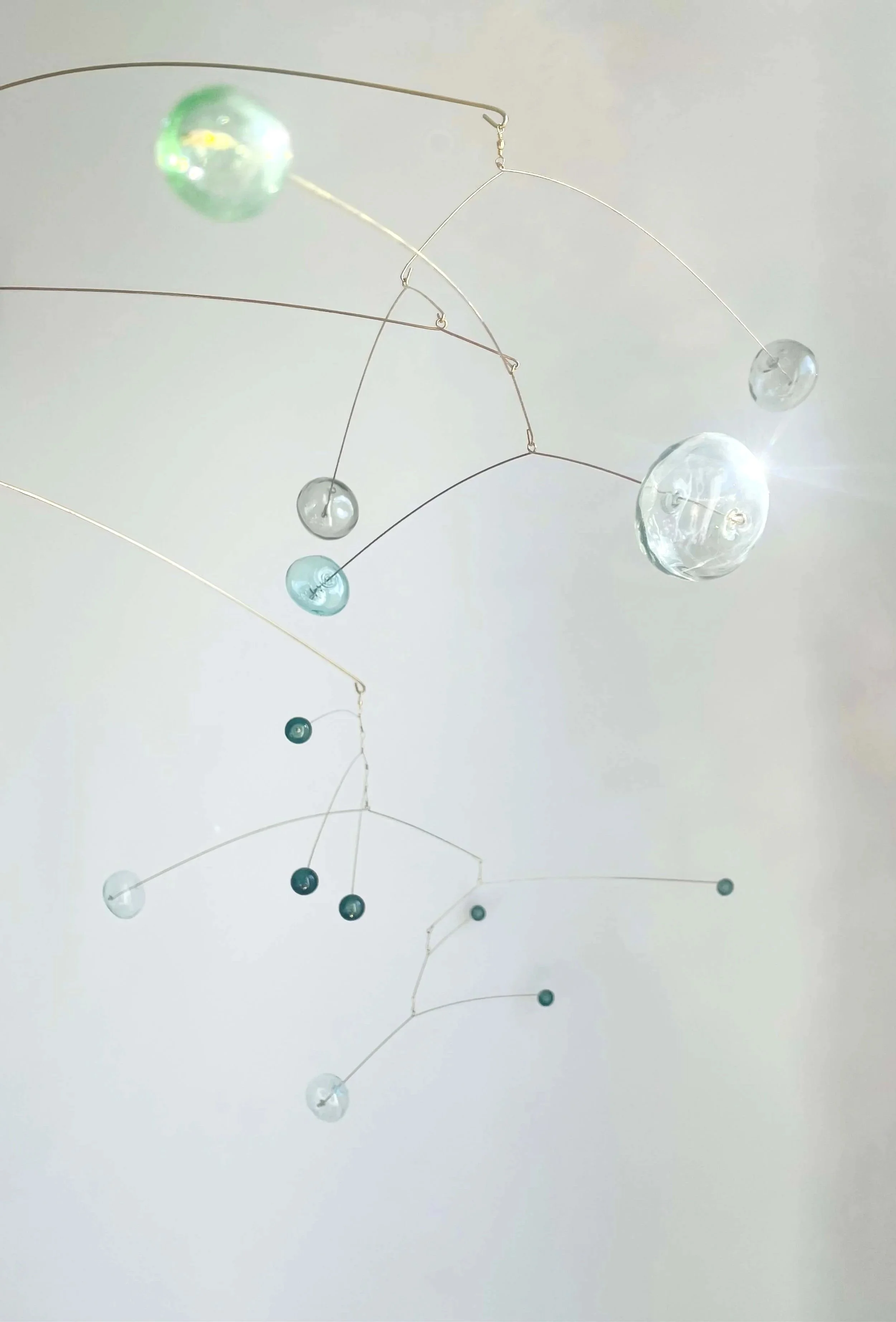 Mobile d'art en fil métallique avec des perles en verre transparentes et bleues, suspendu contre un mur blanc.