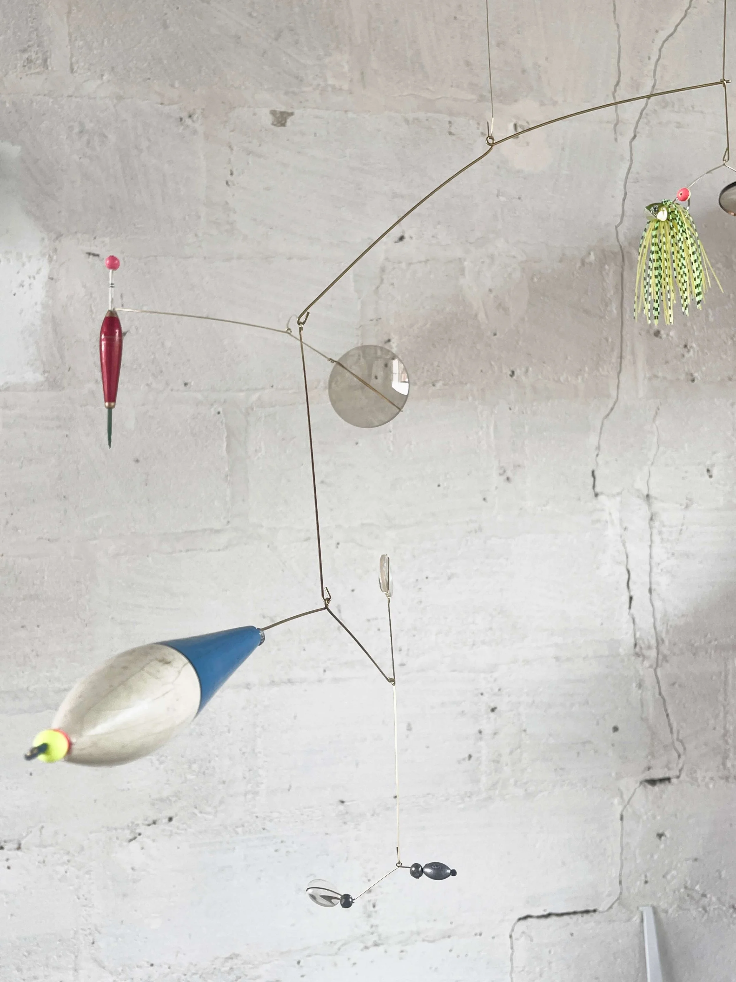Mobile décoratif fait de divers objets suspendus, dont des poissons et des billes, accroché au plafond.