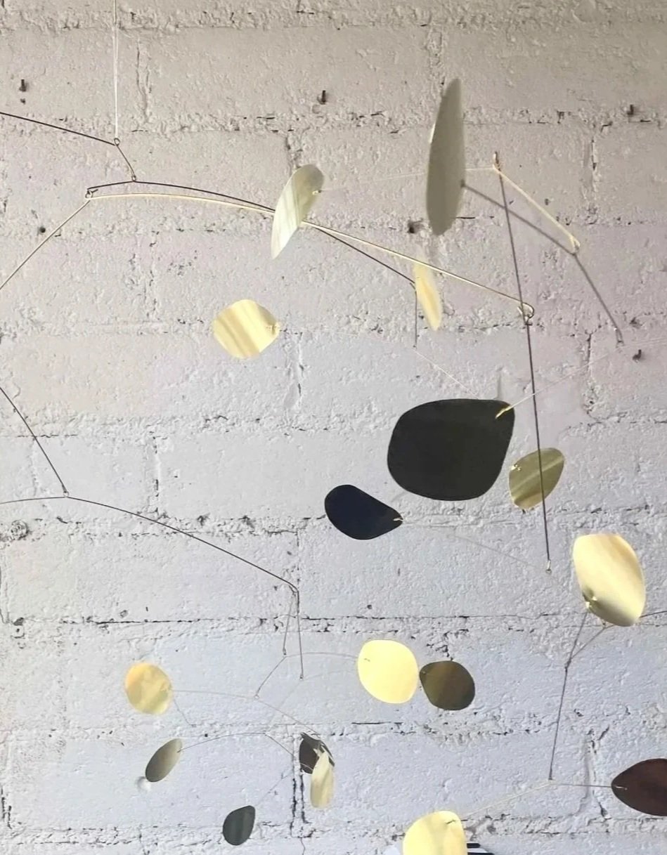 Mobile décoratif suspendu avec des cercles métalliques de différentes tailles en or, noir et argent, contre un mur en briques blanches.