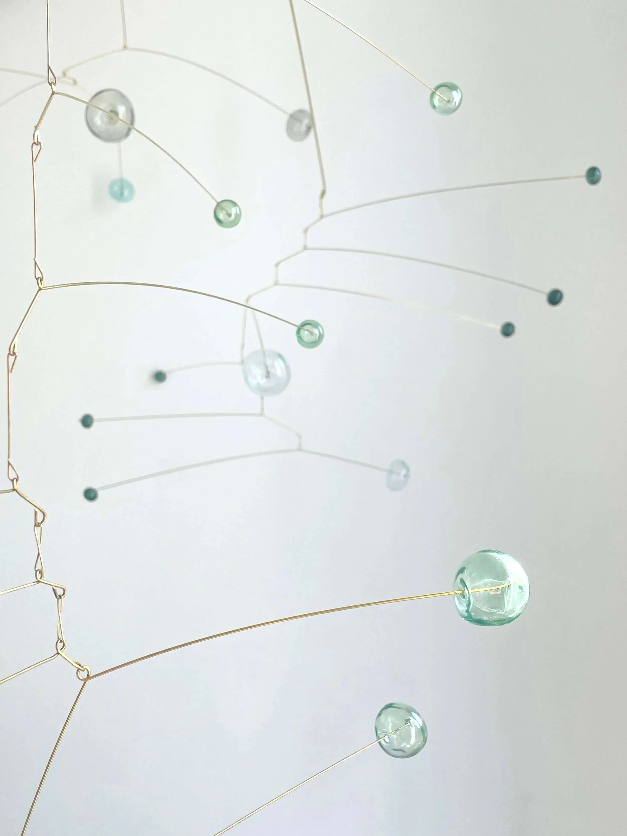 Lustre moderne en fil de métal avec des décorations en verre transparent de différentes tailles, suspendues par des fils métalliques, fixé au plafond blanc.
