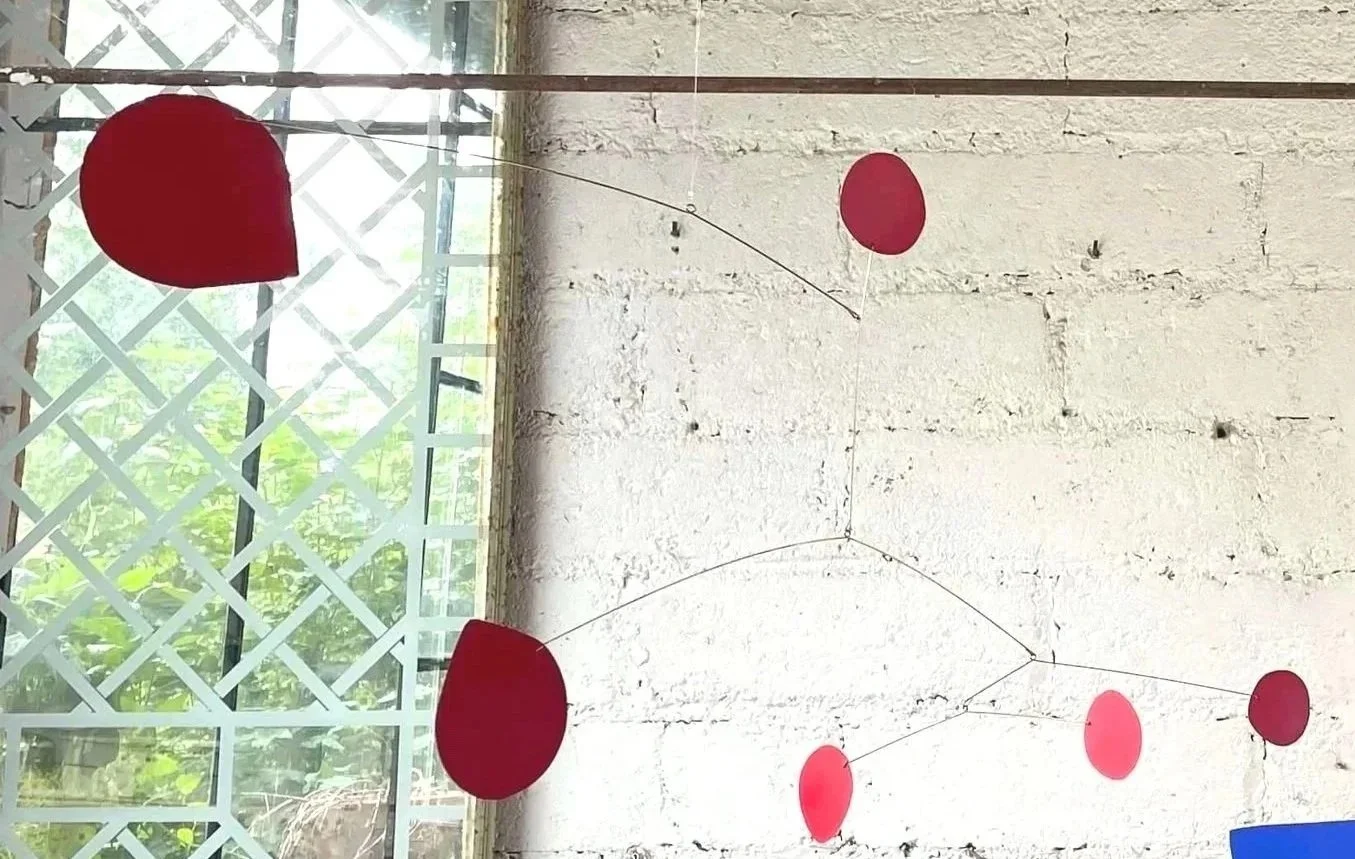 Décoration suspendue composée de plusieurs ballons rouges de différentes tailles attachés par des fils, accrochés au plafond d'une pièce avec un mur en pierre blanche en arrière-plan.
