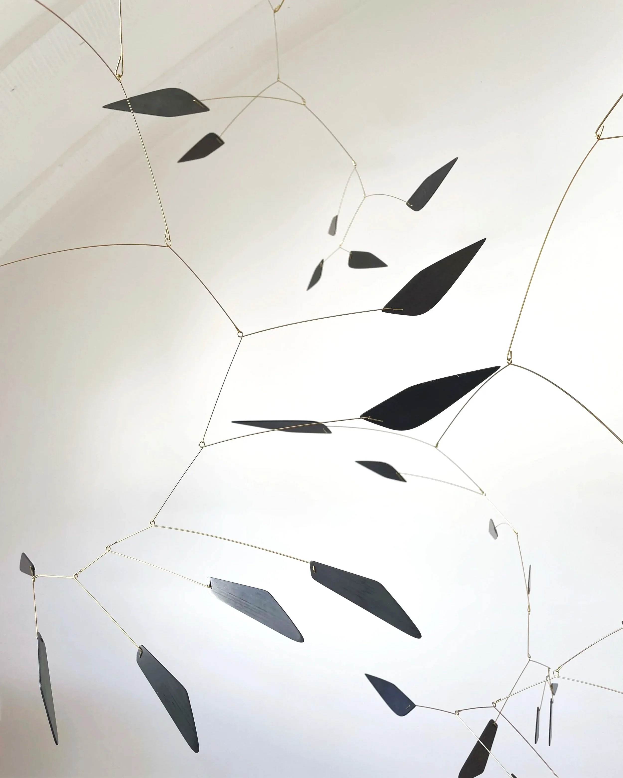 Lustre suspendu avec des éléments en forme de feuilles noires suspendues par des filins délicats en or.