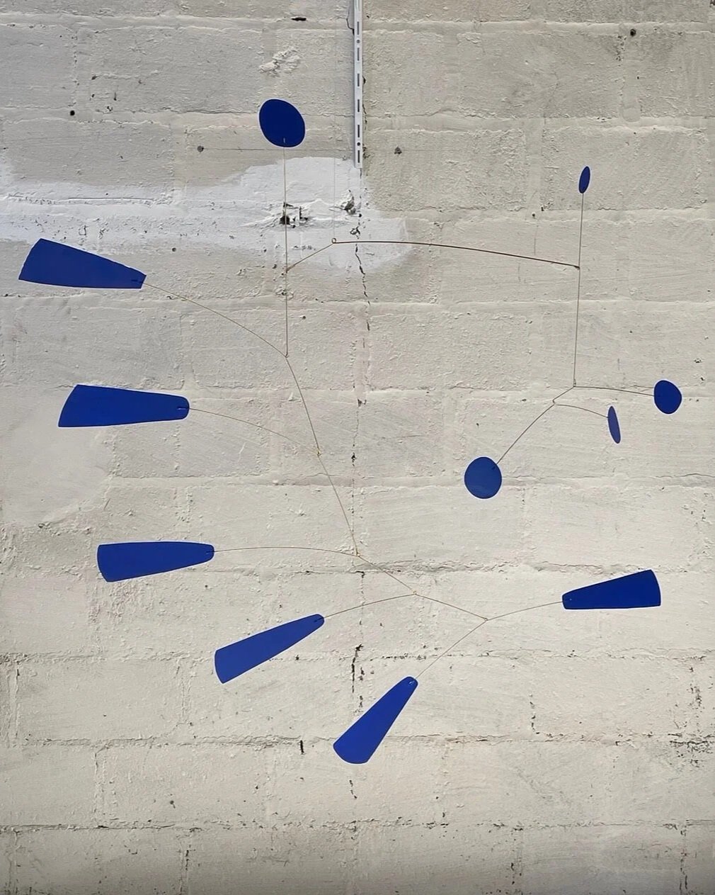segments bleus suspendus par des fils fins, fixée à un mur en briques peint en blanc.