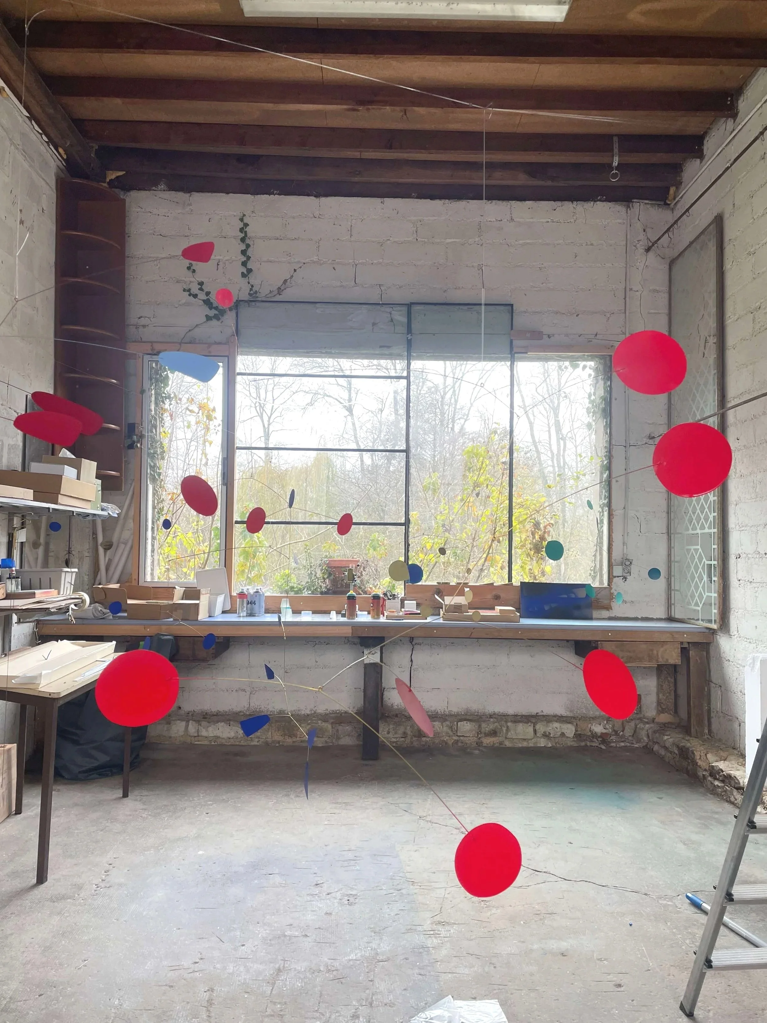 Une pièce en cours de rénovation avec des murs en briques apparentes, un grand vitrage laissant entrer la lumière naturelle, et des décorations suspendues de boules rouges, bleues, jaunes et vertes.