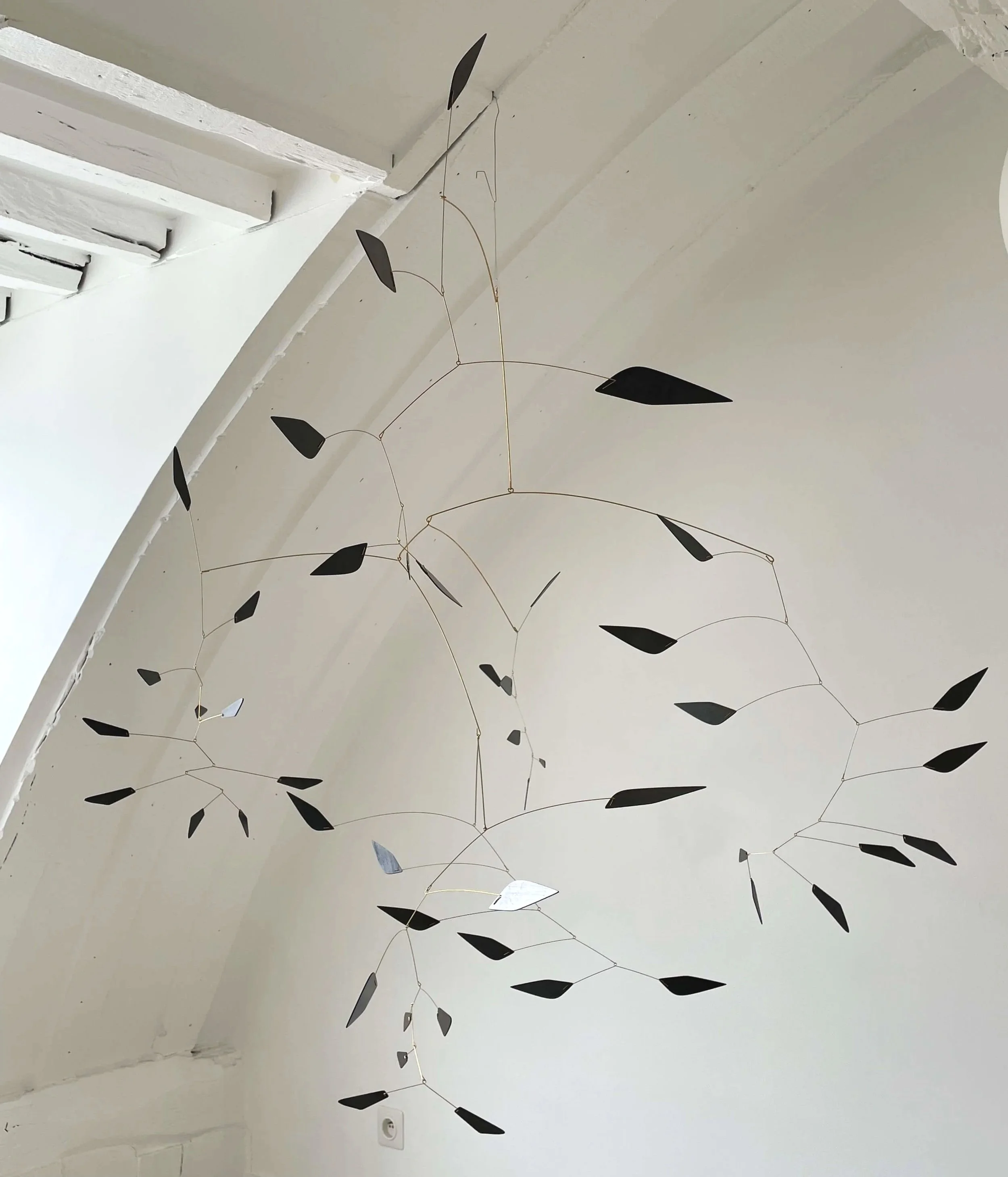 Une décoration suspendue composée de plusieurs motifs noirs en forme de feuilles ou d'ailes en métal, fixés à des fils fins accrochés au plafond blanc.