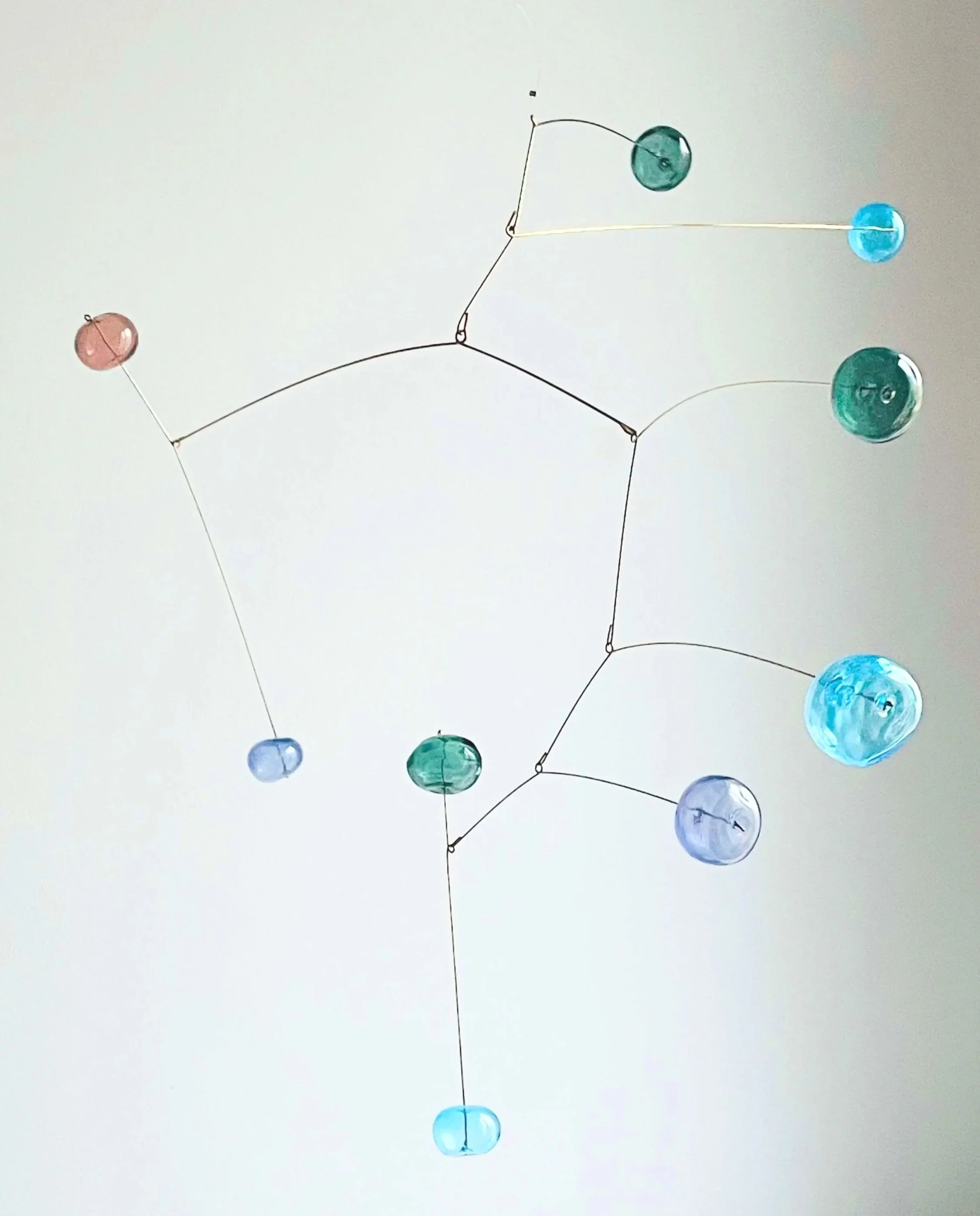 Une suspension artistique composée de boules en verre coloré attachées à des fils noirs formant une structure suspendue.