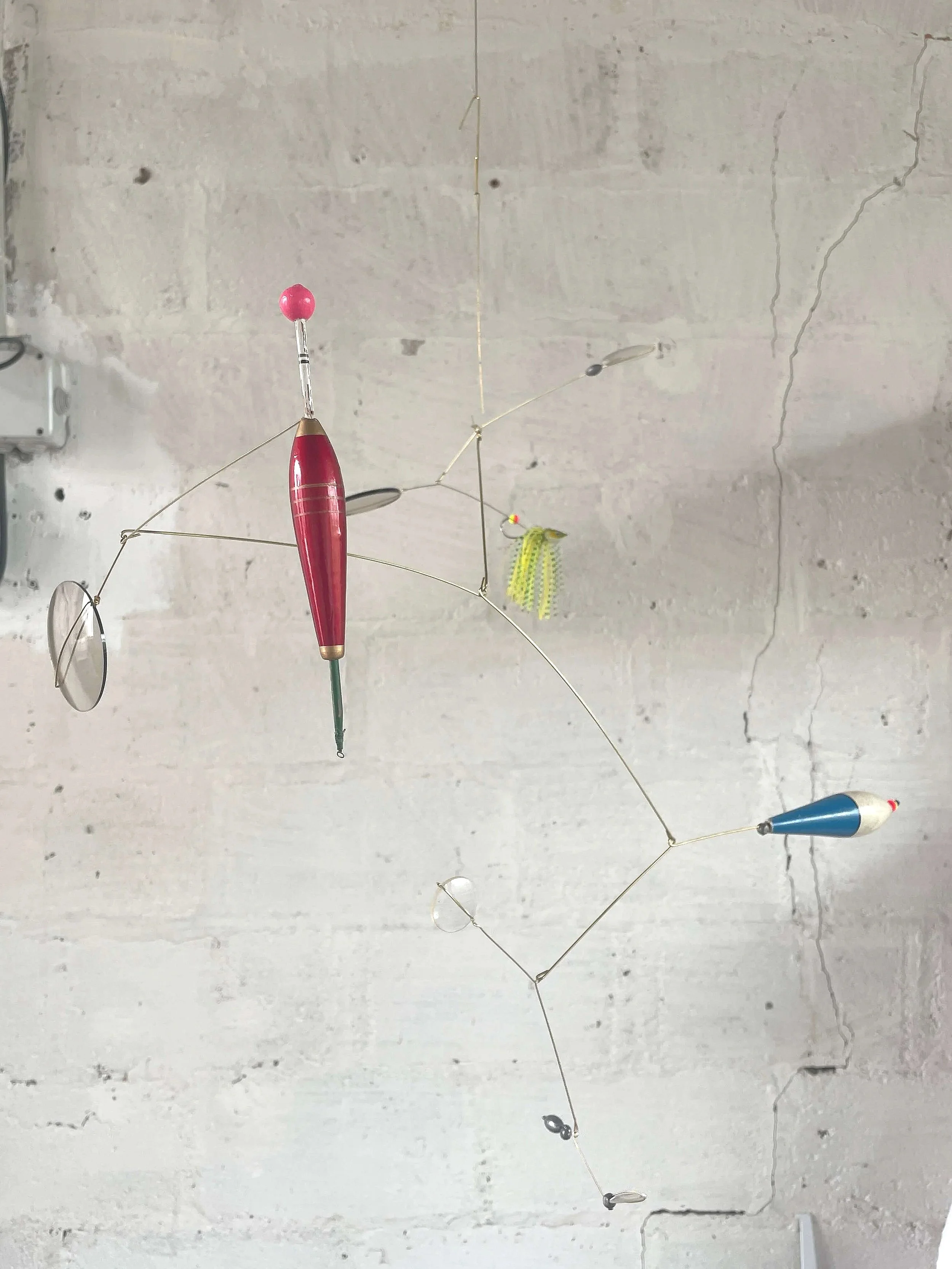 Moulinet artisanal suspendu avec des apparaux de pêche en plastique et un fil métallique, fixé au plafond d'une pièce avec murs en béton