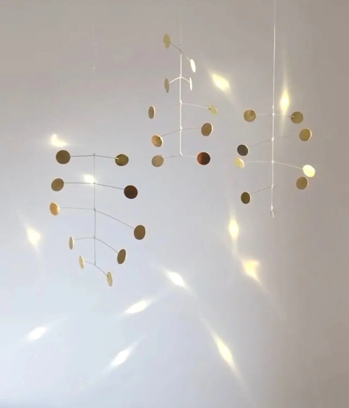 Décoration murale suspendue composée de cercles dorés reliés par des fils, créant une structure en trois dimensions qui projette des reflets lumineux sur le mur.