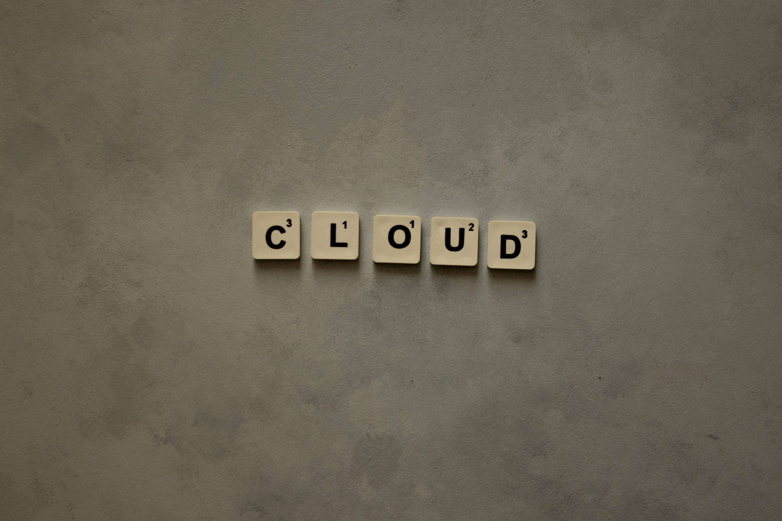 Scrabble-Buchstaben, die das Wort 'CLOUD' bilden, auf einem grauen Hintergrund.