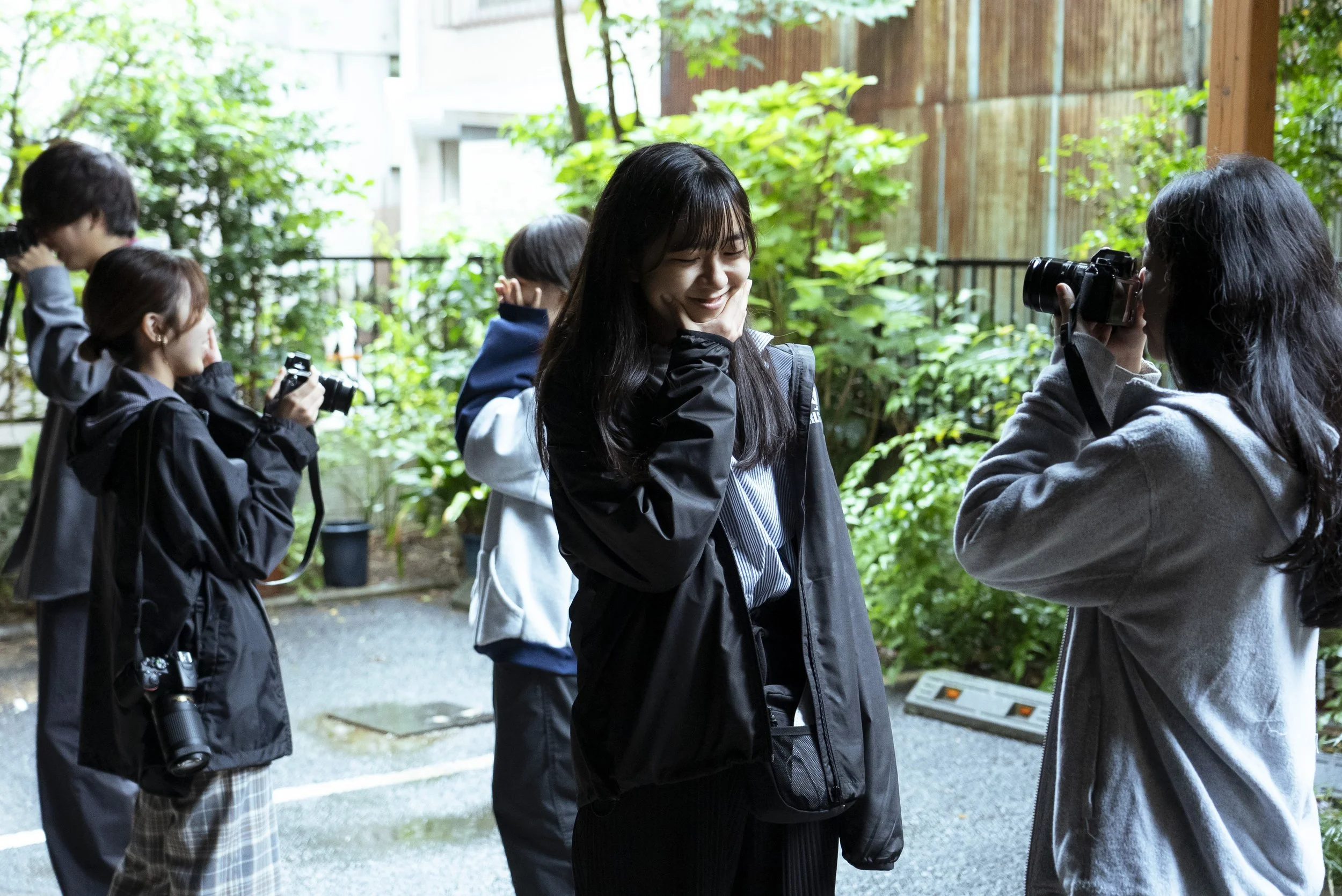 笑っている若い女性を撮影する女性カメラマンと、他のカメラマンたちが周囲にいる屋外の写真