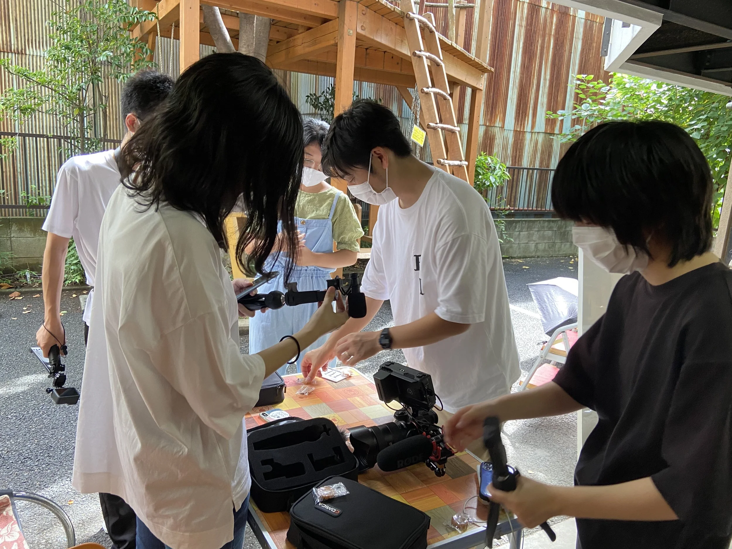 数人の若者が屋外で撮影機材を使って動画や写真を撮っている。