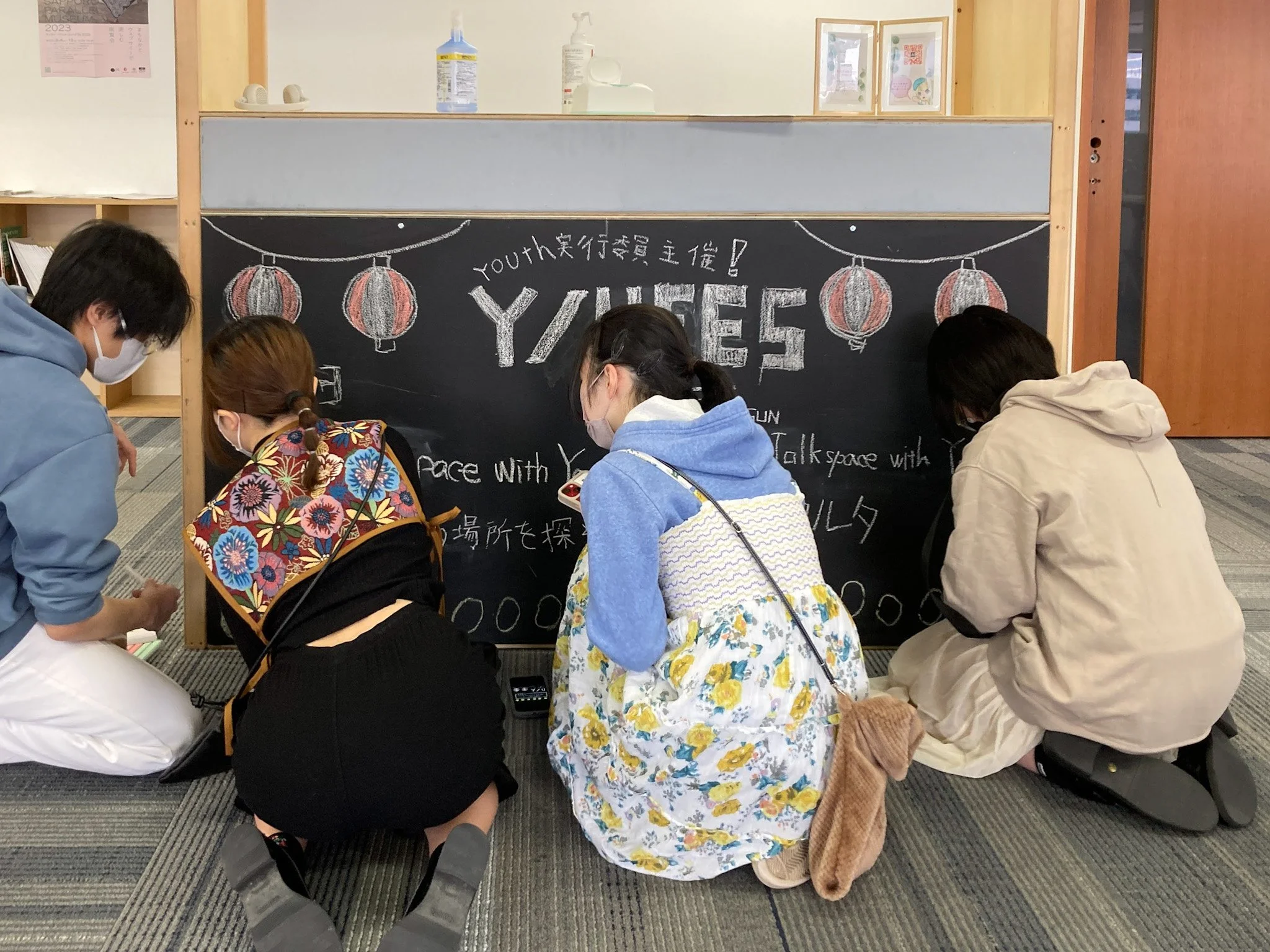黒板にイラストと文字が書かれていて、4人の人がその前で座っている。