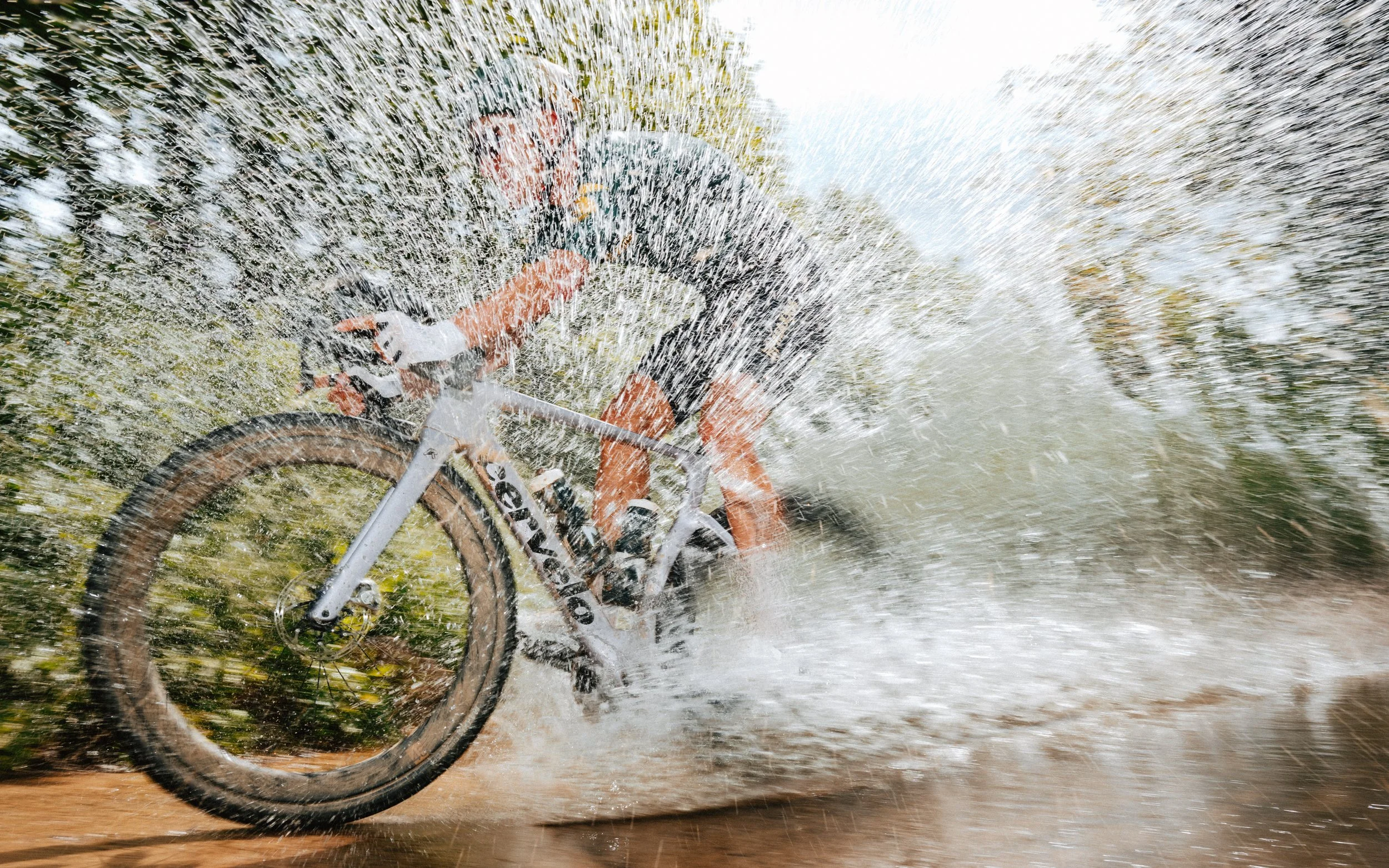 A person riding a mountain bike through water, creating a spray of water around them.