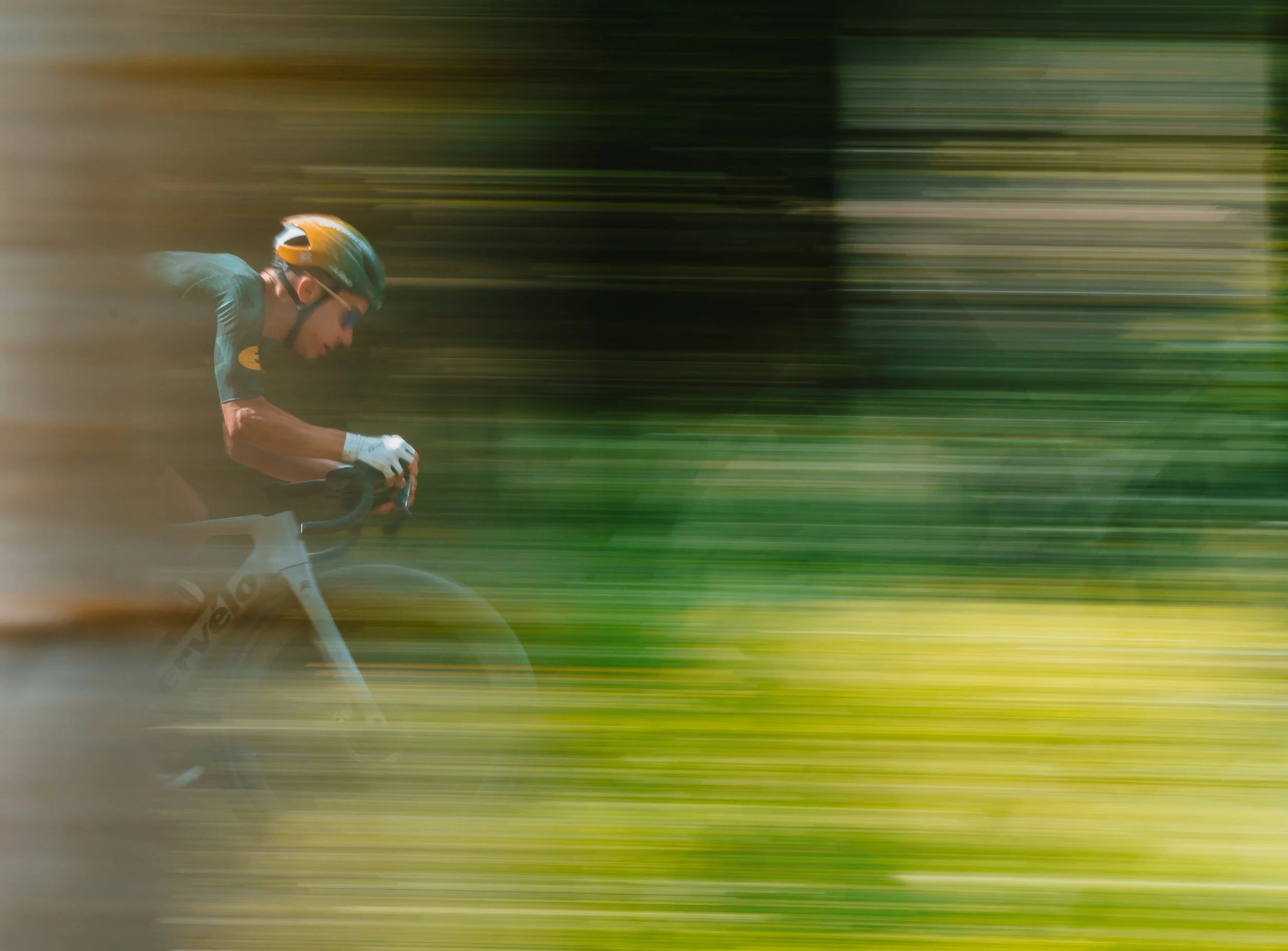 A cyclist wearing a helmet and sunglasses riding a bicycle fast through a nature trail with blurred trees in the background.