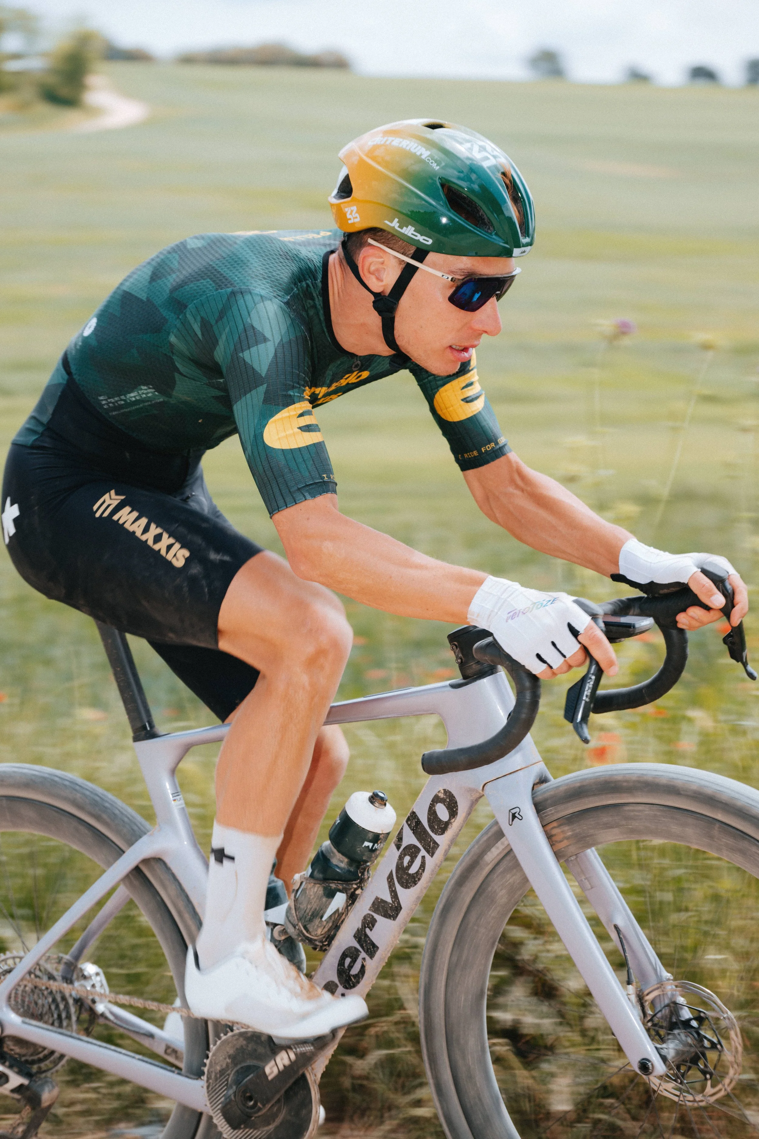 A male cyclist in a racing outfit and helmet riding a racing bicycle outdoors on a grassy trail.