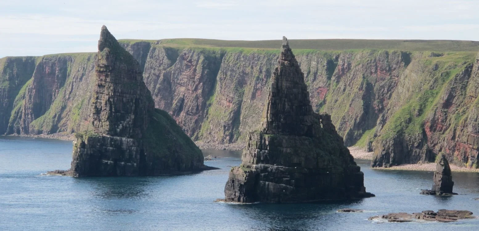 Cliffs and sea stacks along a coastline with green grassy tops and rocky formations in the water.