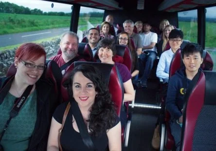 Group of people sitting on a bus, smiling at the camera during a trip.