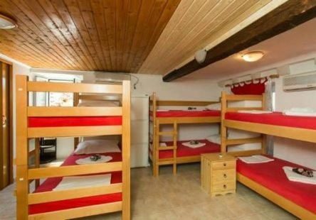 Dormitory room with three wooden bunk beds with red bedding and a small wooden nightstand