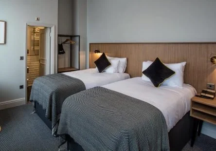 Two twin beds with black pillows and gray bedspreads in a modern hotel room