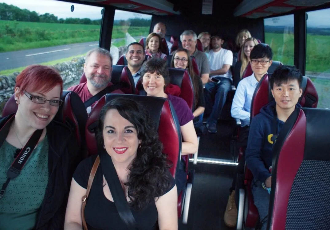 Smiling group of diverse people on a bus traveling through a scenic countryside.