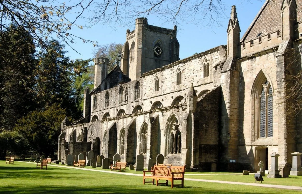 Historic stone church with Gothic windows, surrounded by a grassy area with benches and trees.