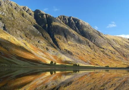 Mountains reflected in a calm lake under a clear blue sky.