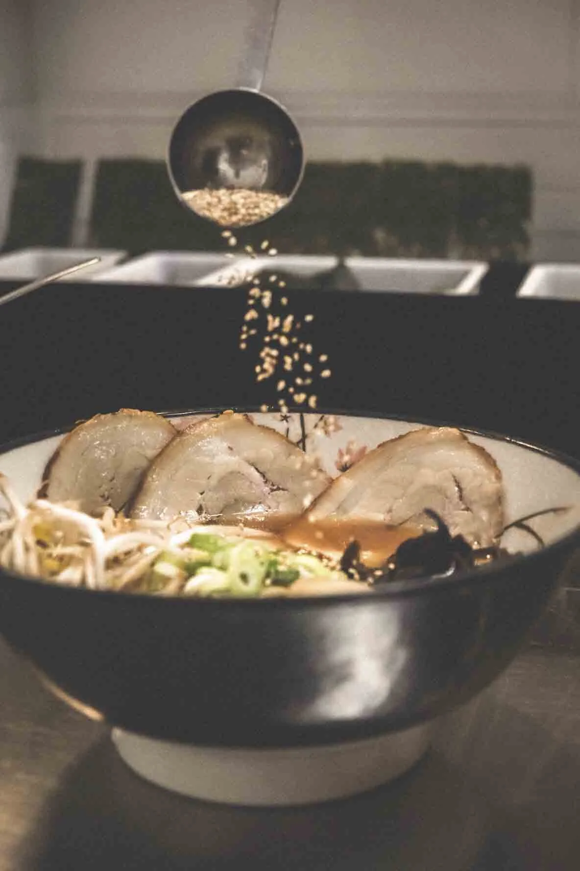 Fond de soupe avec des tranches de viande, des oignons verts, et des ingrédients pour la cuisine asiatique, avec du poivre noir en train d'être saupoudré.