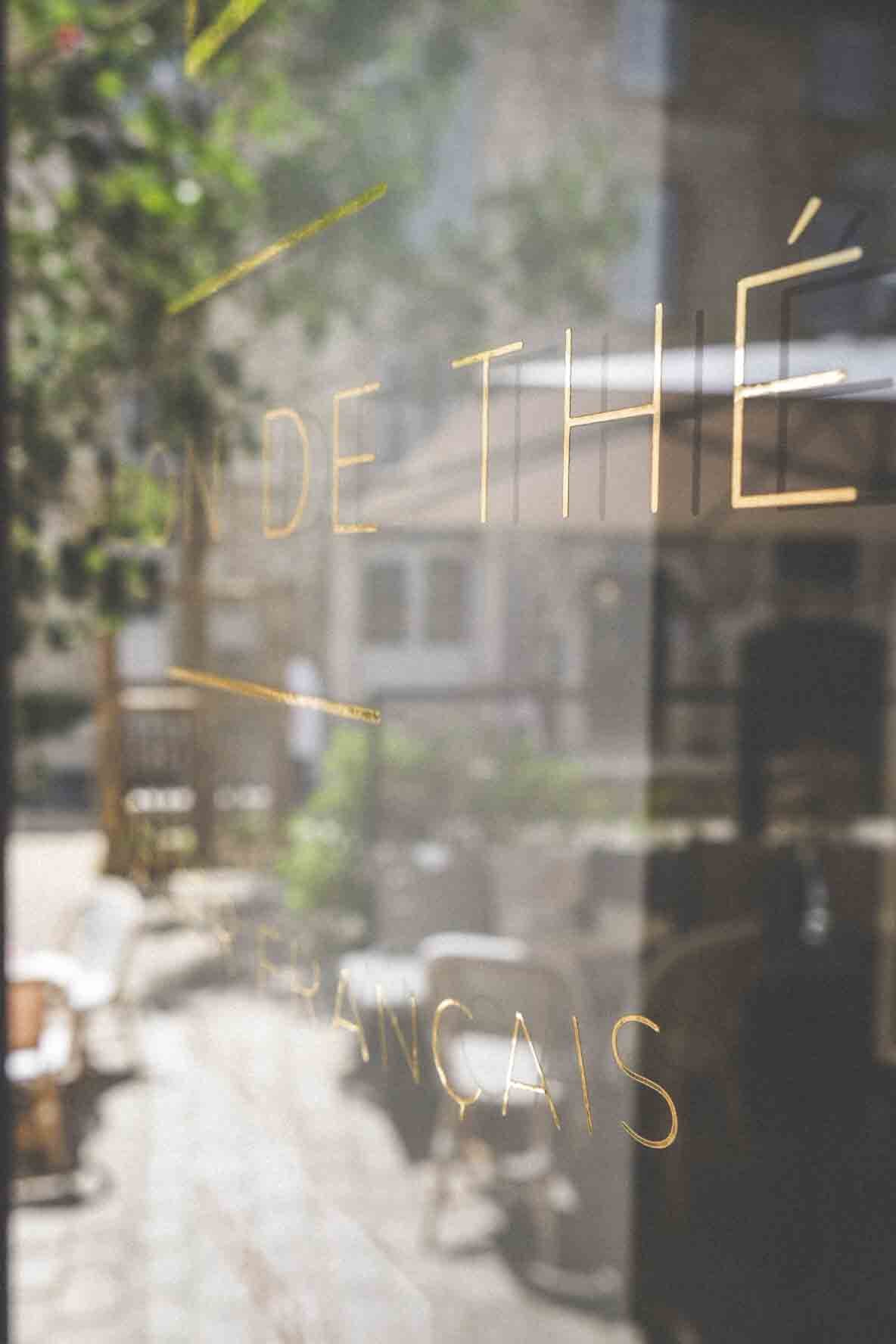 Vue à travers une vitre avec inscription en lettres dorées, montrant une rue avec des voitures et des arbres, ambiance urbaine