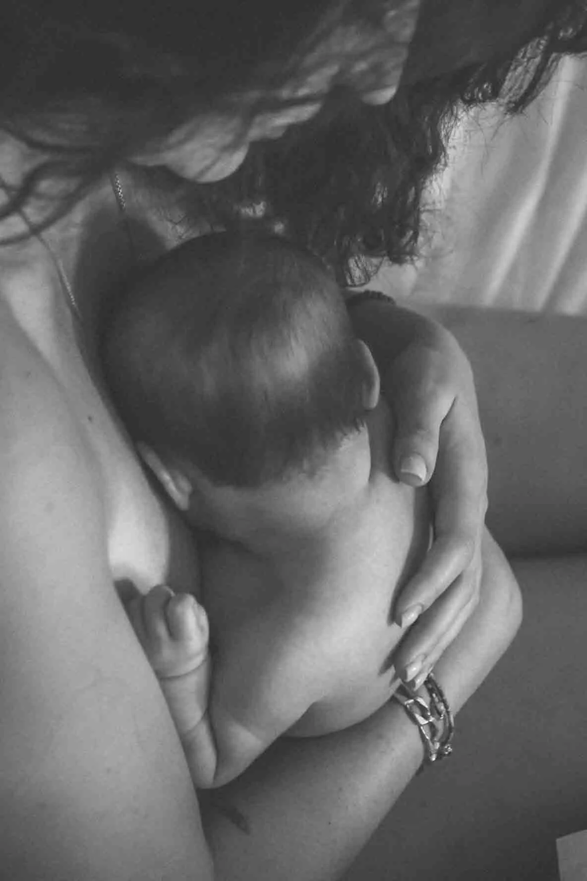 Une femme tient un bébé contre sa poitrine, allaitement en noir et blanc.