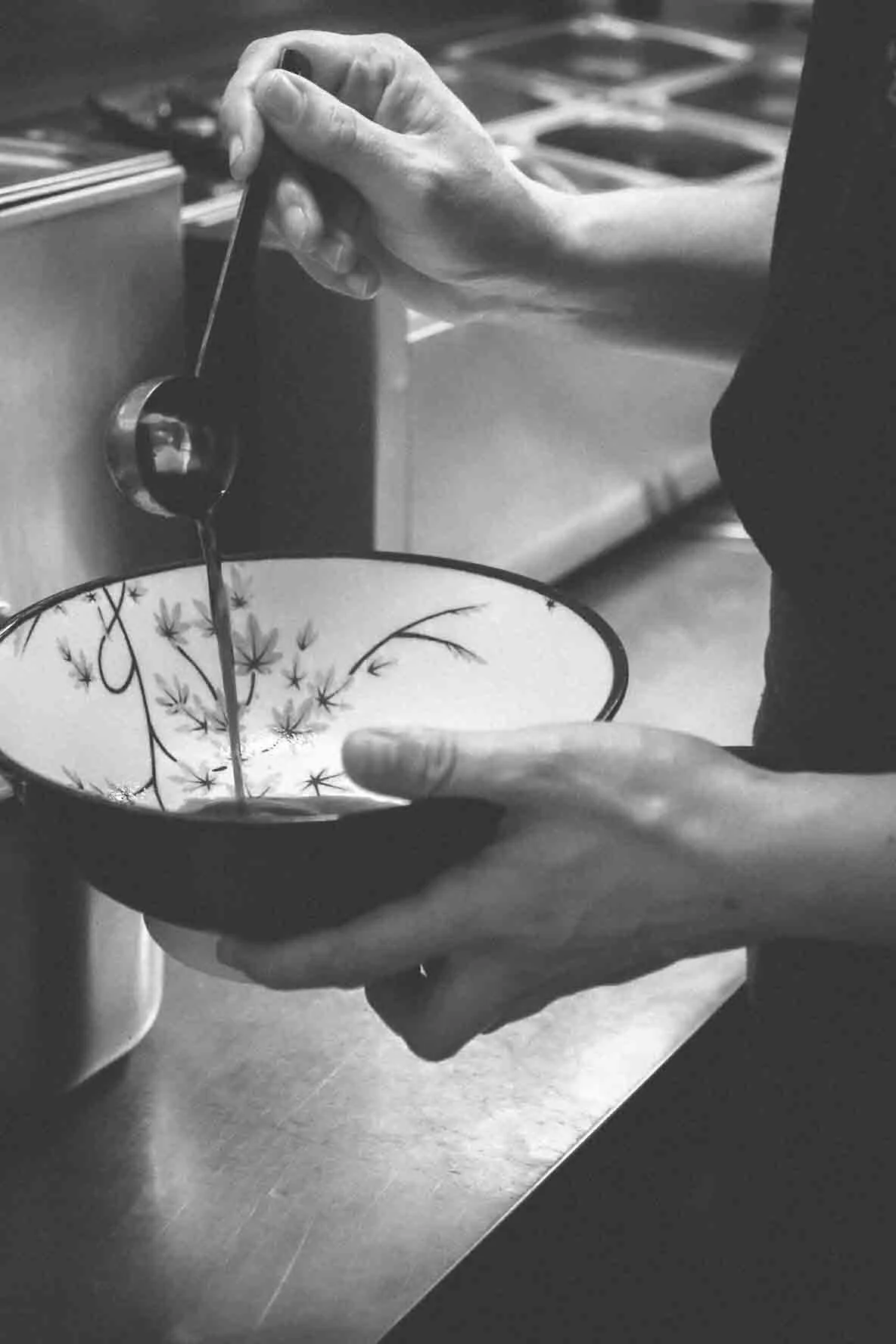 Une personne verse de la sauce dans un bol décoratif avec un motif floral.