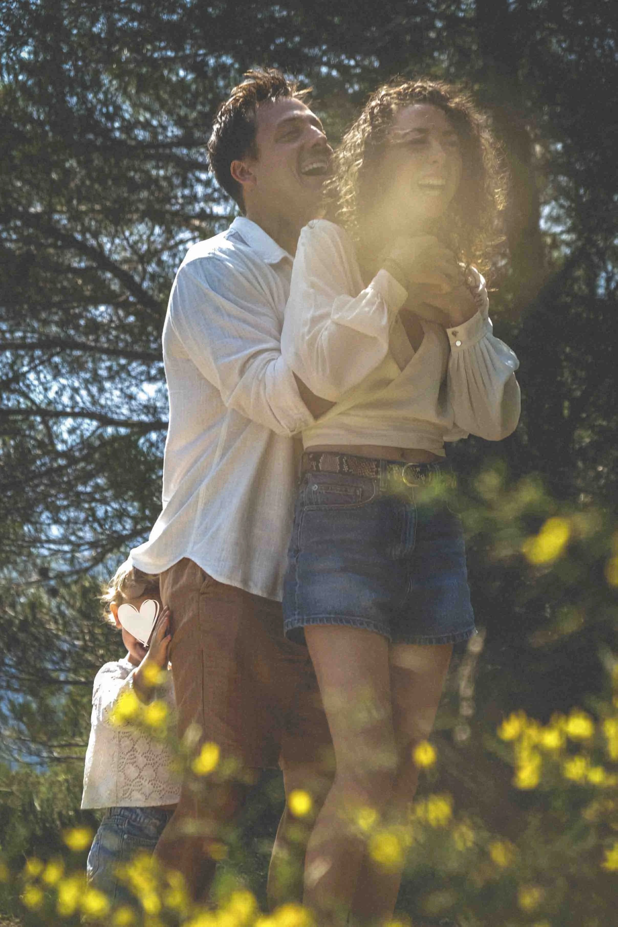 Deux femmes dans un parc en plein air, riant et partageant un moment joyeux ensoleillé, entourées d'arbres et de fleurs jaunes