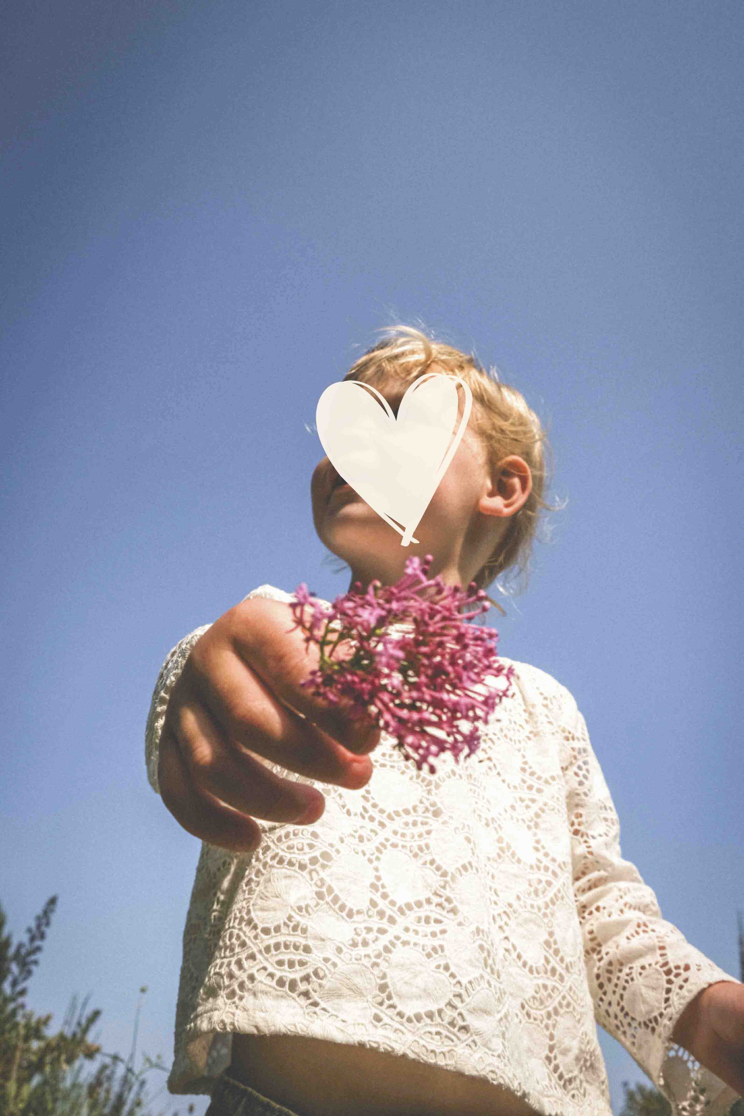 Une jeune fille en blouse en dentelle blanche tient un bouquet de petites fleurs roses, avec un ciel bleu en arrière-plan.