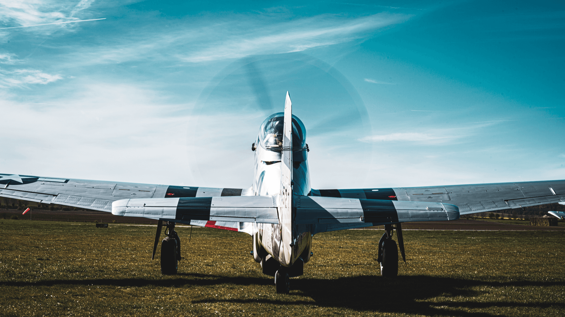 A military jet airplane parked on a grassy airfield under a blue sky with wispy clouds.